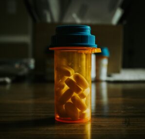 A prescription bottle filled with yellow pills on a wooden table.