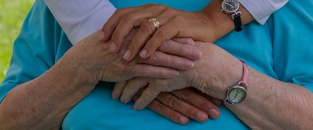 A close-up of two pairs of hands, one older and one younger, gently resting on top of each other, symbolizing compassion