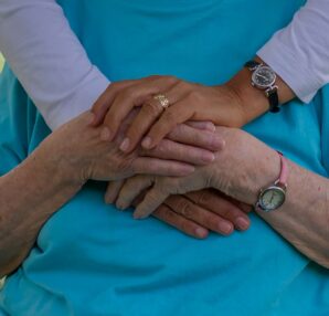 A close-up of two pairs of hands, one older and one younger, gently resting on top of each other, symbolizing compassion
