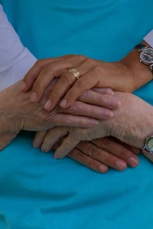 A close-up of two pairs of hands, one older and one younger, gently resting on top of each other, symbolizing compassion