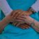 A close-up of two pairs of hands, one older and one younger, gently resting on top of each other, symbolizing compassion