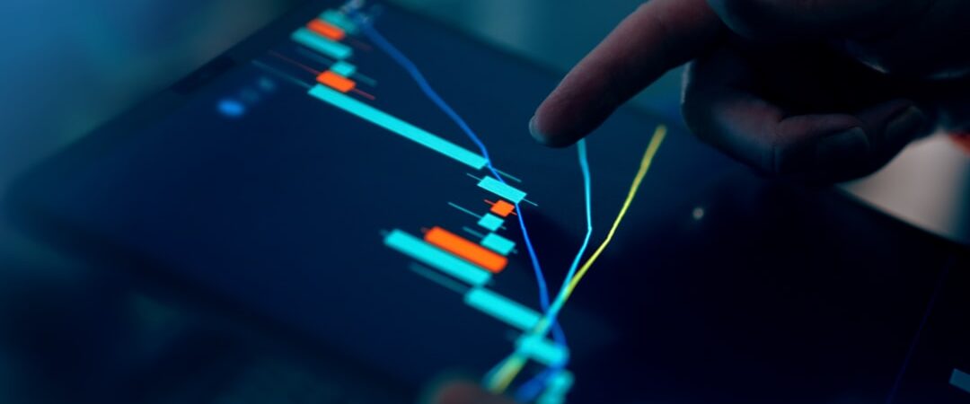 Close-up of a hand pointing at a stock market graph on a tablet screen