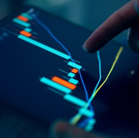 Close-up of a hand pointing at a stock market graph on a tablet screen