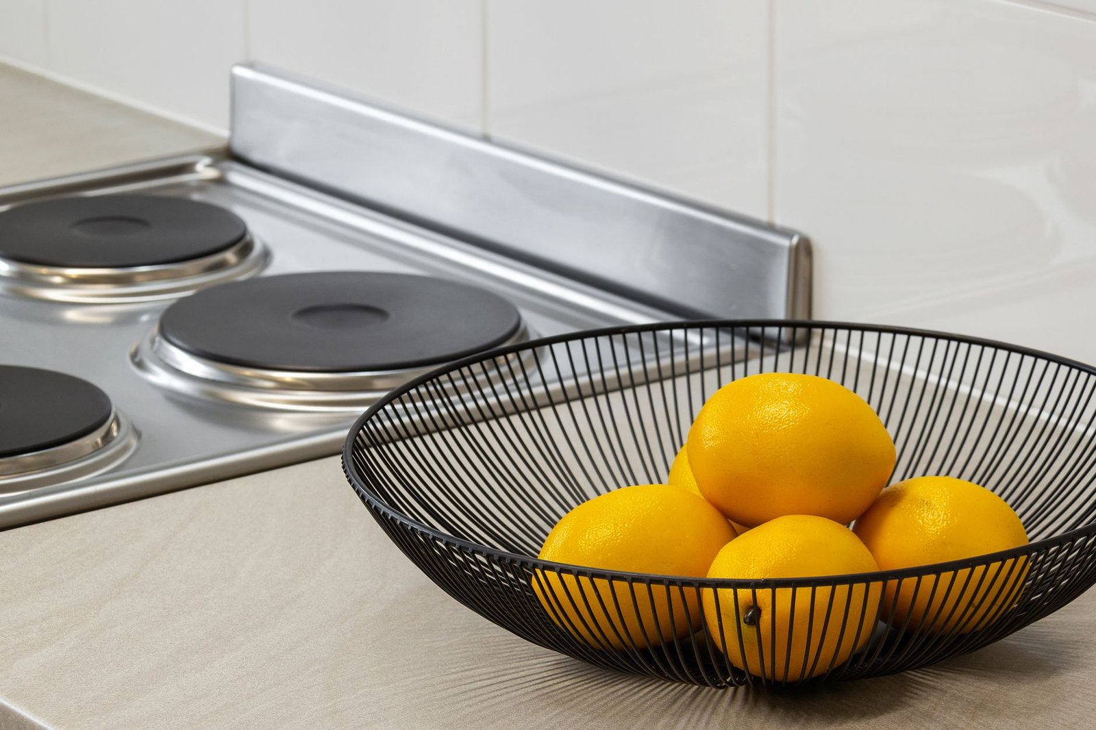 Lemons in a metal bowl on a kitchen counter beside an electric stove, highlighting freshness and simplicity. — Benefits of We