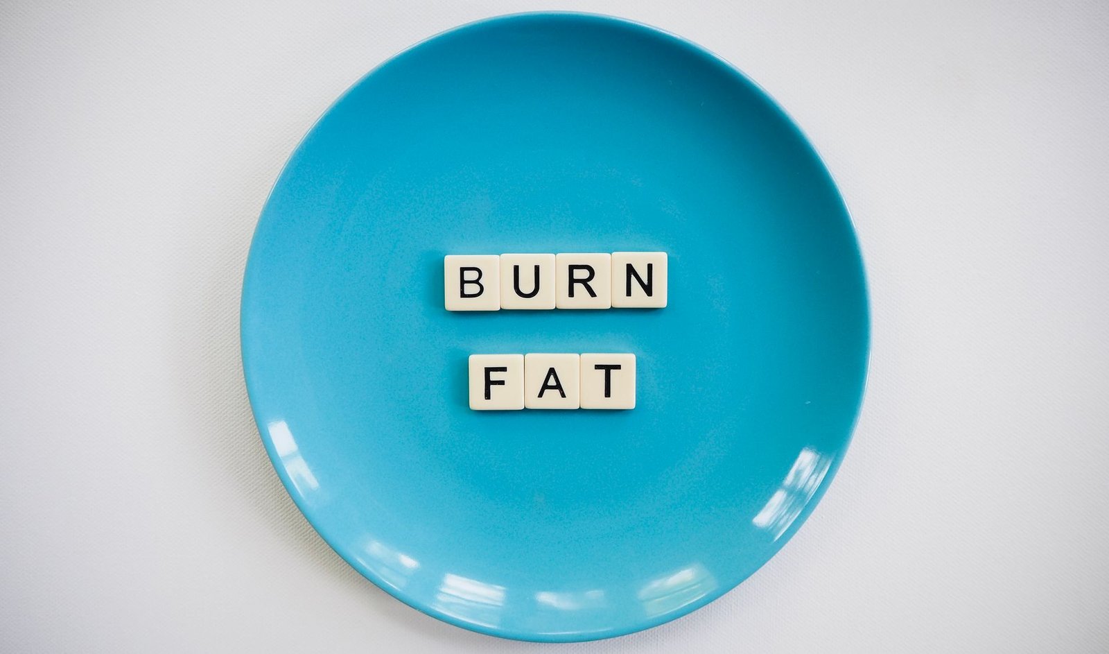 A conceptual image featuring the words 'Burn Fat' on a blue plate, symbolizing weight loss. — Consuming less calories And Wei