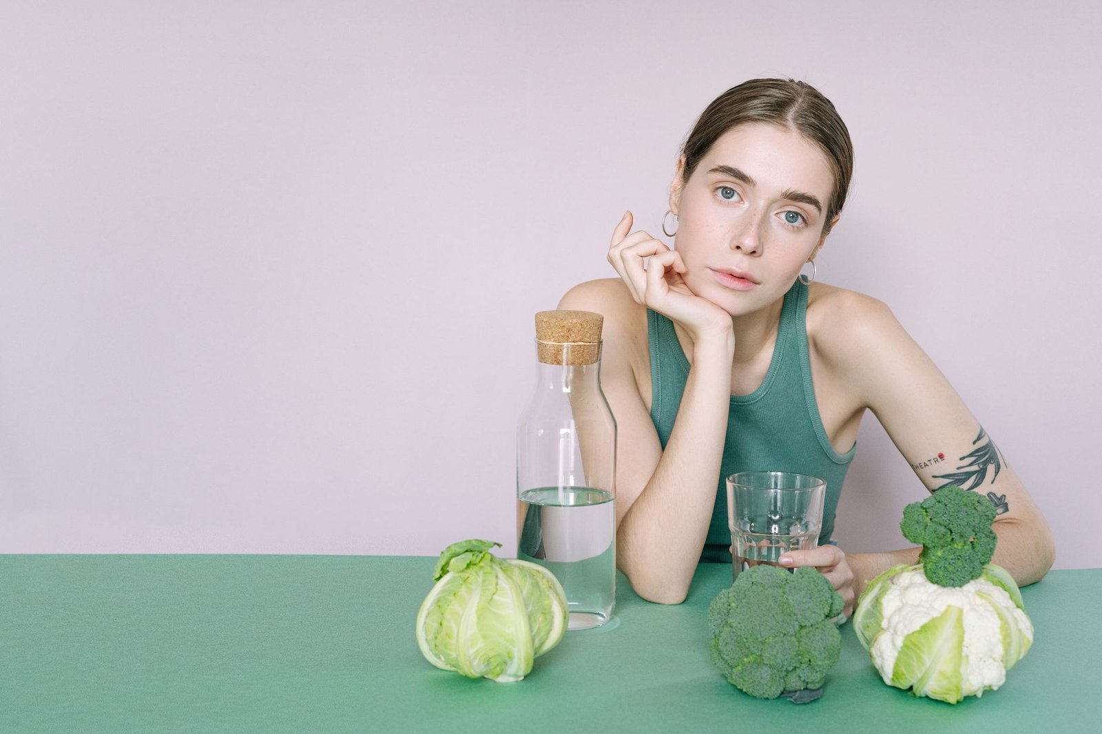 A young woman in a green top sitting with vegetables and a glass of water. — EODD Diet Reviews - 5 Things I Like About Jon Be
