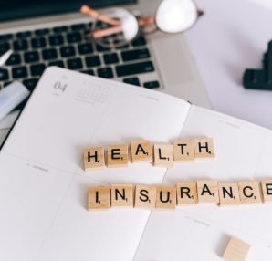 Close-up of Scrabble tiles spelling 'Health Insurance' on a planner with a laptop. — Glo Yoga Online for People With Busy Sch