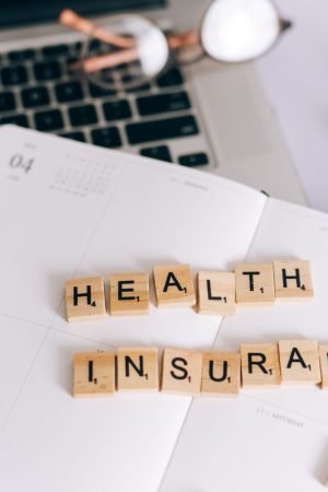 Close-up of Scrabble tiles spelling 'Health Insurance' on a planner with a laptop. — Glo Yoga Online for People With Busy Sch