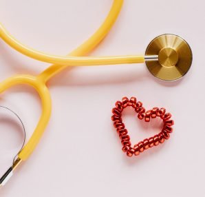 Top view of yellow stethoscope made of plastic and metal material near small handmade heart of spiral hair tie on pale pink b