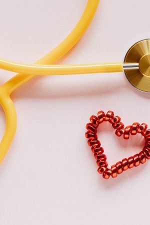 Top view of yellow stethoscope made of plastic and metal material near small handmade heart of spiral hair tie on pale pink b