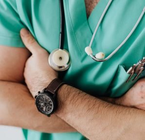 Unrecognizable man wearing medical uniform with stethoscope and pens standing in hospital with crossed arms during work in da