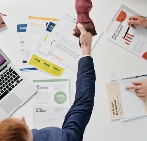 Business professionals engaging in a handshake over a desk filled with financial documents and a laptop. — Relax and Recharge