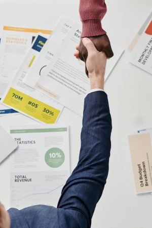 Business professionals engaging in a handshake over a desk filled with financial documents and a laptop. — Relax and Recharge