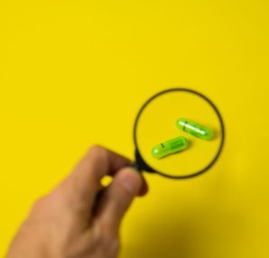 From above of crop unrecognizable male holding magnifying glass over green pills on yellow background in studio — Smart Choic