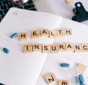 Scrabble tiles spelling 'Health Insurance' on planner with pills and laptop, symbolizing healthcare planning. — Smartest Choi