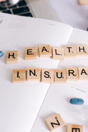 Scrabble tiles spelling 'Health Insurance' on planner with pills and laptop, symbolizing healthcare planning. — Smartest Choi